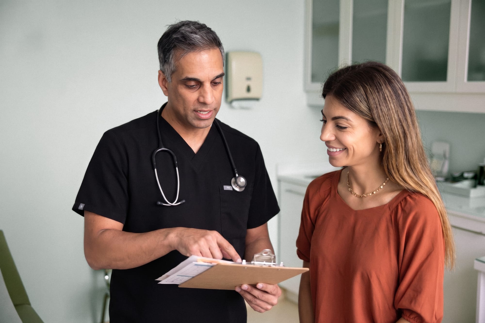 Evolved Medical physician in black scrubs reviewing a clipboard with a smiling patient in the clinic